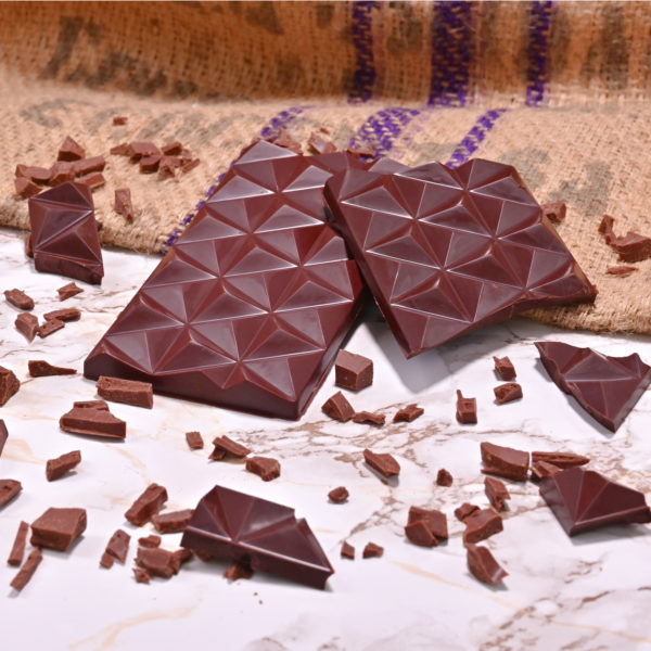 Foto einer dunklen Schokoladentafel von Chani Schoggi in Luzern. Die zwei Tafeln liegen auf einem Jutesack und Marmorboden. Die Schokolade wurde Bean-to-Bar hergestellt.